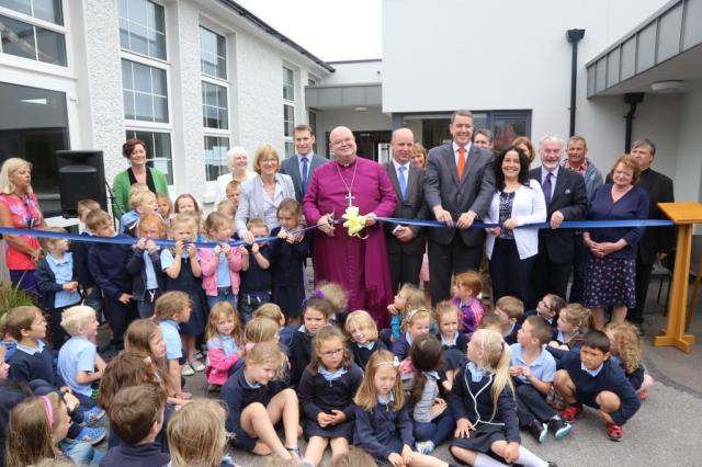 Junior Infants, guests and local politicians help the Bishop with the official opening.  From left (and third to the right of the Bishop) are: Mrs Dorothy Verplancke, Mrs Harriet Pritchard (Principal), Councillor James O'Donovan, the Bishop, Jim Daly, T,.D., Michael McCarthy, T.D. Councillor Margaret Murphy-O'Mahony, and Andrew Coleman (Chairperson of the Board of Management). Photo:  Trevor Collins